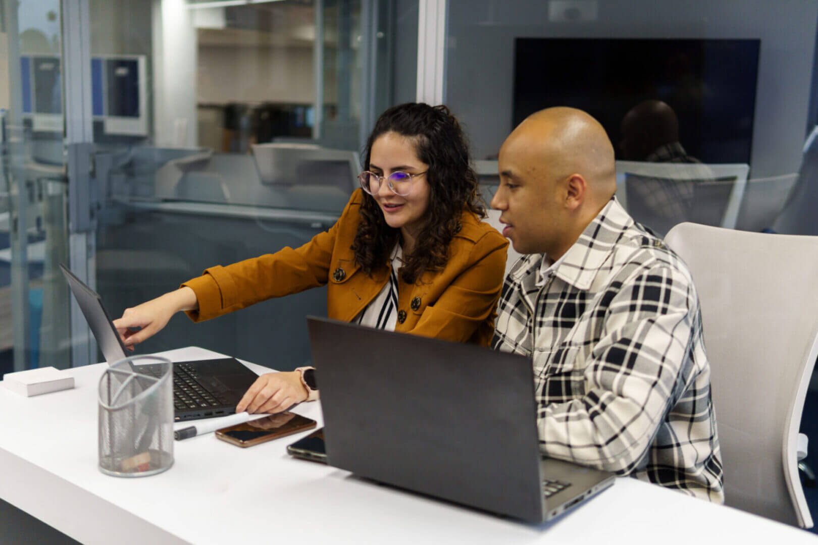 Two colleagues collaborating on laptops in office.